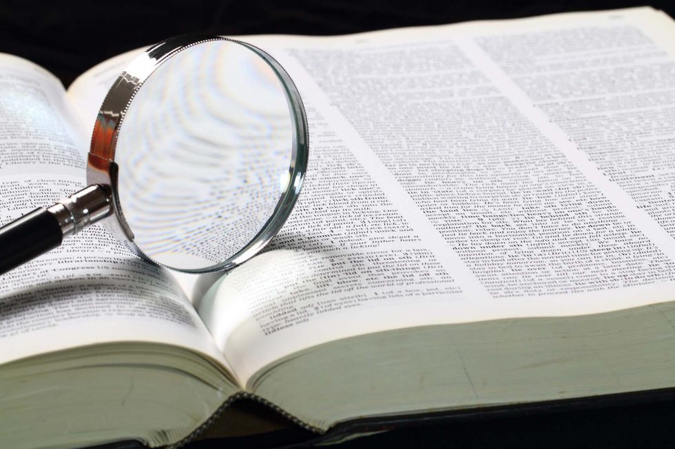 Fotografía de un diccionario abierto con una lupa encima, simbolizando la búsqueda del origen y significado de palabras en inglés.