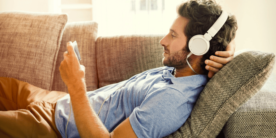 Persona aprendiendo inglés con YouTube desde el sofá utilizando auriculares y un teléfono móvil.
